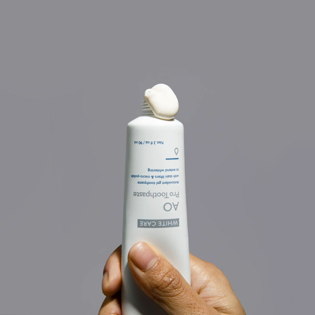 Hand holding Post-Whitening Toothpaste tube upside down with a dollop of white gel paste squeezed from the opening