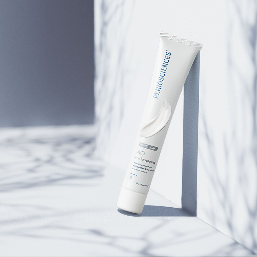 PerioSciences AO ProToothpaste tube leaning against marble surface with a white gel swatch on the packaging