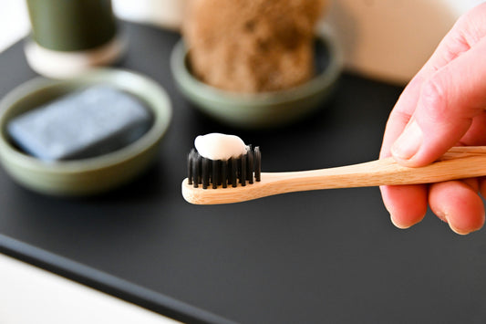 A hand holding a bamboo toothbrush with toothpaste on it. Photo by Nik on Unsplash.